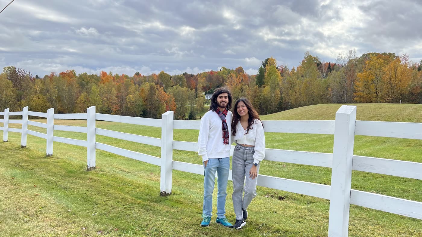 Abirami and Prateek by a white fence on an autumn afternoon